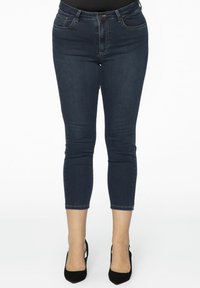 Donkerblauwe denimjeans met een slim fit, middelhoge taille en cropped lengte. Voorzien van een klassiek 5-pocket ontwerp en stikseldetails.