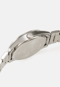 Orologio in acciaio inossidabile argentato con cassa rotonda, lunetta testurizzata e cinturino a bracciale, con superficie lucidata e corona laterale.