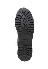 Zwarte rubberen zool van een laars met een uitgesproken loopvlakpatroon met kruisvormen en ribbels voor grip. Inclusief merknaam "TRAVELIN."