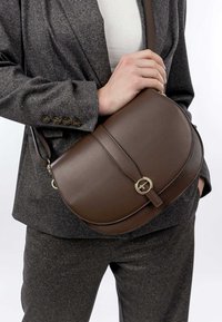 Borsa a tracolla in pelle marrone con alette curve, hardware dorato e tracolla slim regolabile. La borsa presenta linee pulite e dettagli minimi.