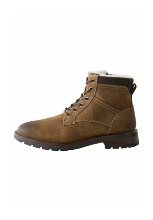 Braune Wildleder-Stiefelette mit Schnürdesign, weißem Fellfutter am oberen Rand und einem strukturierten schwarzen Akzent. Gummisohle mit Grip-Muster.