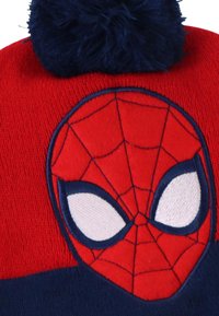 Rode gebreide beanie met een marineblauwe pompon, met een geborduurd Spiderman-gezicht met witte ogen en zwarte webdetails.