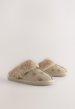 Chaussons beiges avec un revers en fausse fourrure, présentant une extérieure douce, des motifs animaliers en relief, et une semelle en caoutchouc profilée basse.