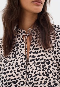 Leopardi-kuosiset puserot pehmeää kangasta, jossa on suljettu avainreikäkaulus, sitottuna lenkillä. Värimaailma koostuu beigestä ja mustasta.