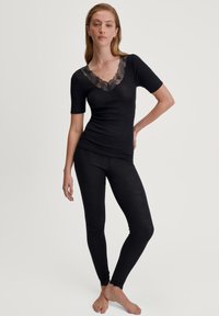 Top corto nero a maniche corte con collo a V bordato in pizzo, abbinato a leggings neri. Il tessuto sembra leggero e aderente con una texture liscia.
