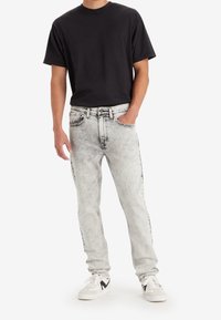 Svart crew-neck t-shirt, ljus tvättade denimjeans med blekt mönster, med rak ben och synlig sömnad. Ett par vita sneakers.