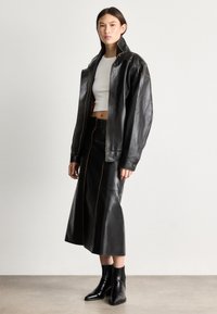 Μαύρο δερμάτινο oversized μπουφάν με πορτοκαλί ραφές, συνδυασμένο με μαύρη δερμάτινη midi φούστα και μυτερές μαύρες μποτάκια μέχρι τον αστράγαλο. Λείο υλικό.