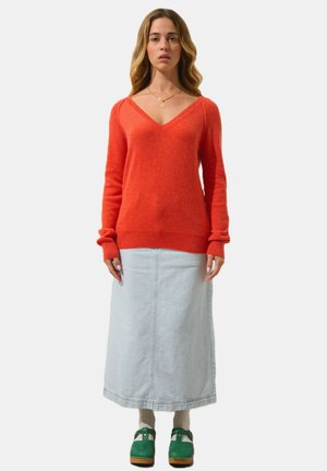 Pull en mélange de laine rouge avec un col en V, associé à une jupe maxi en denim bleu clair et des sabots verts. Manches courtes avec des poignets côtelés.