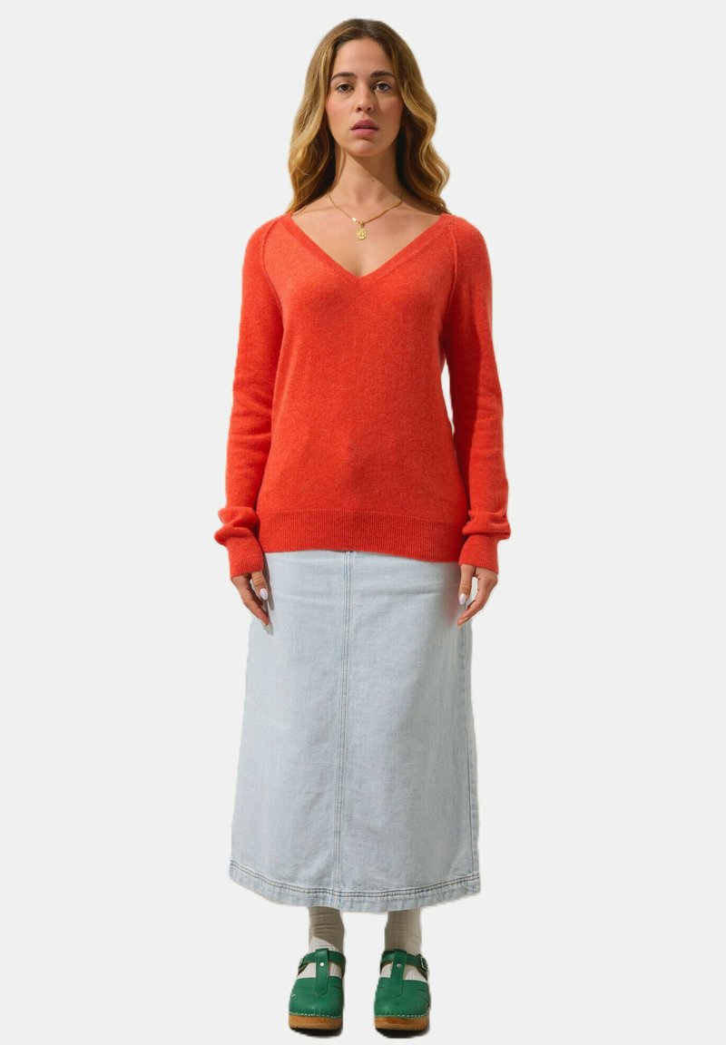 Roter Wollmischpullover mit V-Ausschnitt, kombiniert mit einem hellblauen Jeans-Maxikleid und grünen Clogs. Kurze Ärmel mit gerippten Bündchen.