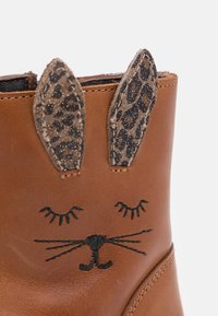 Stivale in pelle marrone con una faccia di gatto ricamata, con baffi in filo nero e occhi chiusi, sormontato da orecchie in stampa leopardata beige.