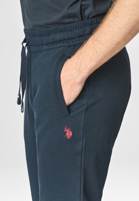 Jogging in misto cotone blu navy, con vita elastica e cordoncino. Sulla tasca sinistra c'è un piccolo logo ricamato rosso. Inclusi tasche laterali.