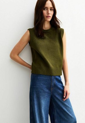Olive green sleeveless sweater with a textured surface, paired with wide-leg blue denim jeans. Simple design, modern silhouette.
