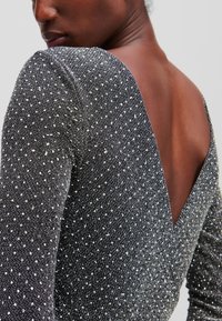 Melnā un sudraba garā piedurkne apģērba ar dziļu V-veida aizmuguri, kas izgatavots no teksturētas auduma, rotāts ar mazām, atstarojošām punktiem.