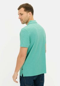 Türkises Kurzarm-Polohemd mit Kragen, seitlichen Schlitzen und weichem Material, getragen mit dunklen Jeans, von hinten betrachtet.