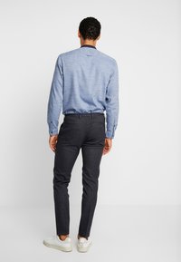 Světlomodrá košile na knoflíky s dlouhými rukávy, nošená s tmavě šedými kalhotami slim fit a bílými teniskami, pohled zezadu.