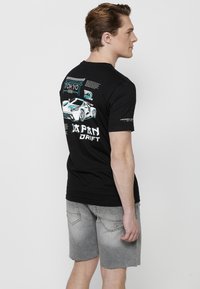 Juodas medvilnės marškinėliai su sportinio automobilio grafika, ant nugaros raudona spalva užrašas "TOKYO" ir storu baltu šriftu "JAPAN DRIFT".