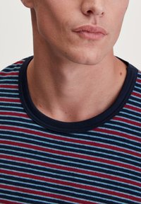 T-shirt en coton rayé avec un col rond côtelé bleu marine. Présente des rayures alternées bleues et rouges sur fond sombre.