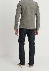 Grå, letvægtsjakke med skulderlapper, parret med mørkeblå jeans og beige sneakers. Synlig syning og lomme detaljer.