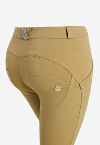 Leggings color khaki con una texture liscia, un design aderente, cuciture curve e una piccola etichetta logo vicino alla tasca posteriore.
