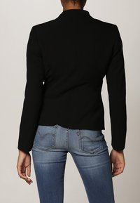 Svart skräddarsydd kavaj med långa ärmar, skräddarsydd design och slät textur, kombinerad med ljusblå denimjeans med rundade bakfickor.