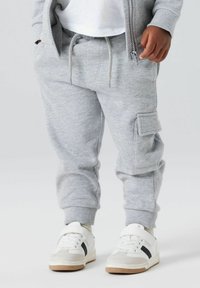 Sive bombažne trenirke z elastičnimi manšetami, pasom na vrvico in stranskimi žepi. Ujemajo se z belimi športnimi čevlji z belimi detajli.