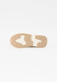 Suola di scarpa con una base in gomma marrone, caratterizzata da profonde scanalature e un inserto bianco, progettata per trazione e durata.