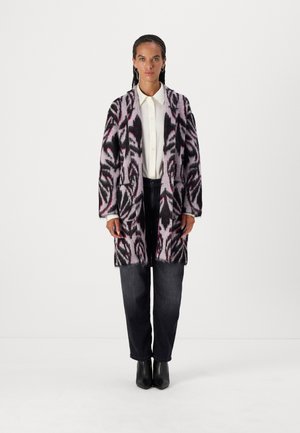 Strickcardigan mit einer weichen Textur, einem abstrakten Muster in Pink, Schwarz und Grau, langen Ärmeln und Seitentaschen. Über einem weißen Hemd getragen.