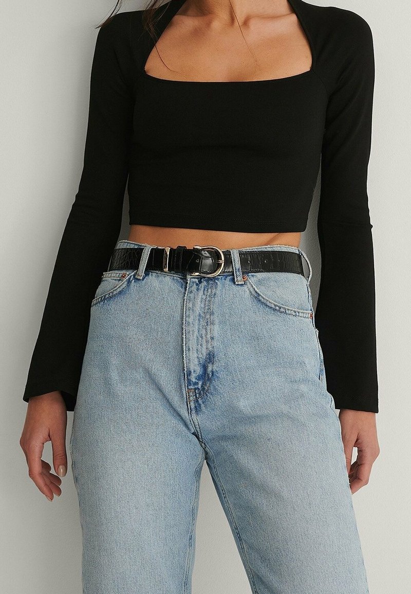 Svart långärmad crop top med fyrkantig urringning, matchad med högmidjade ljusblå denimjeans och ett svart strukturerat bälte med en silverfärgad spänne.