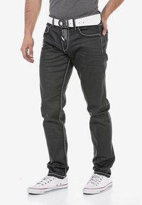 Zwarte denim jeans met witte stiksels, met een witte riem met een decoratieve gesp, gedragen met witte sneakers. Slanke pasvorm.