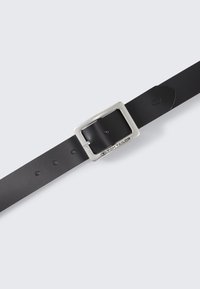 Mustade nahast vöö, millel on ruudukujuline hõbedane metallist pandla ja mitu avad suuruse reguleerimiseks. Logot on nähtav pandlal.