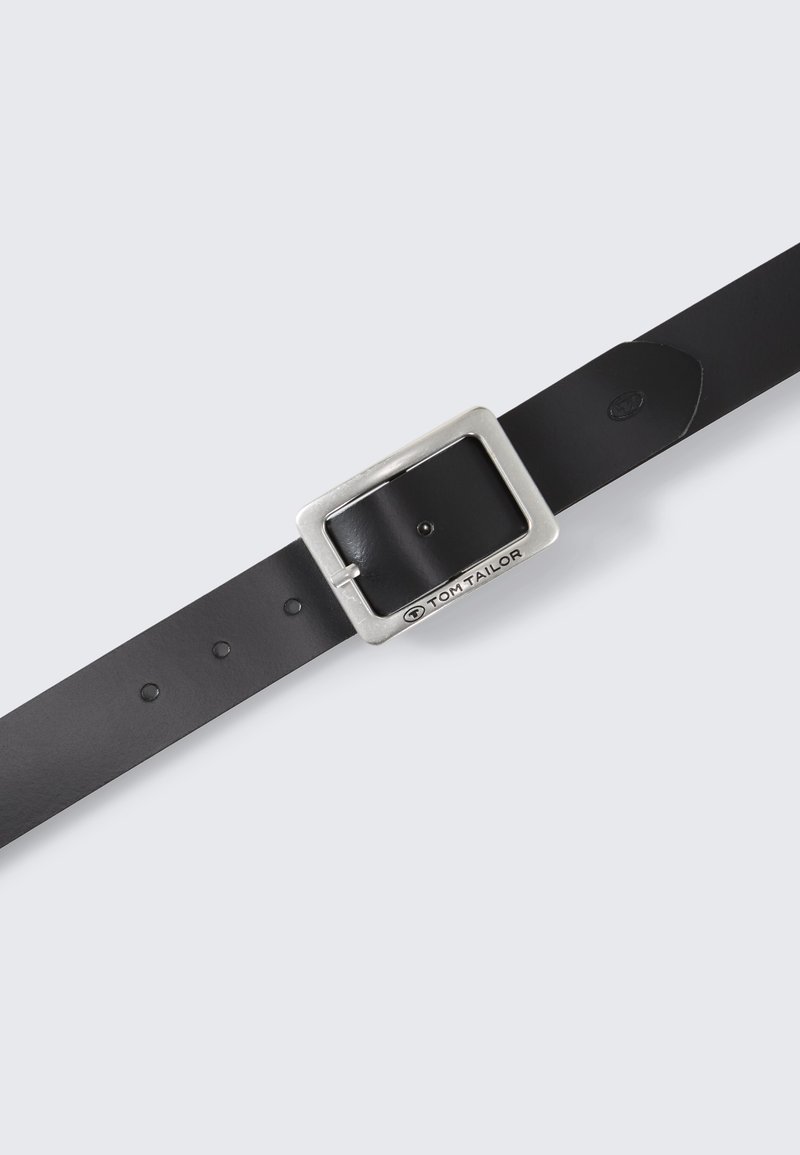 Mustade nahast vöö, millel on ruudukujuline hõbedane metallist pandla ja mitu avad suuruse reguleerimiseks. Logot on nähtav pandlal.