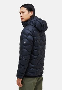 Navy puffer jacket with a zigzag quilted design, hood, and silver logo detail on the sleeve. Made of shiny, synthetic material.
