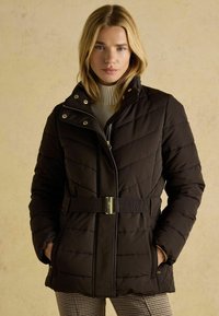 Čierna prešívaná bunda so zipsom a patentkami, vysokým golierom a opaskom v páse. Obsahuje diagonálne švy a bočné vrecká.