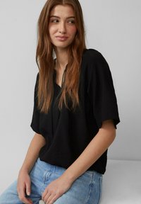 Top noir à manches courtes en tissu léger, avec une coupe décontractée et un col en V, associé à un jean en denim bleu clair.