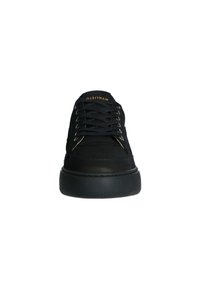 Baskets noires avec un bout arrondi, semelle en caoutchouc texturé, œillets en métal et fermeture à lacets. Elles présentent un upper en synthétique lisse et un logo de marque subtil.