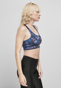 Sportsbh med et blått og lilla pixelerte mønster, laget av elastisk stoff, med brede stropper og en kort design; parret med svarte ribbede leggings.