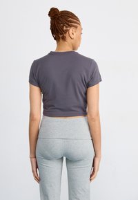 Grijze cropped t-shirt met korte mouwen, gemaakt van zachte stof, gecombineerd met lichtgrijze leggings. Soepele textuur, minimalistisch ontwerp en geen grafische details.