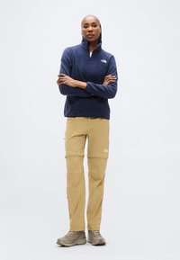 Ναυτικό μπλούζα από φλις με ημιδιακοπή γιακά, σε συνδυασμό με χακί παντελόνι cargo με φερμουάρ στα γόνατα, φορεμένο με γκρι παπούτσια πεζοπορίας.