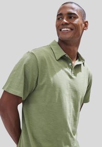 Kurzärmliges Polohemd in hellgrün, aus glattem Stoff mit klassischem Kragen, Knopfleiste mit drei Knöpfen und einer dezenten Textur.