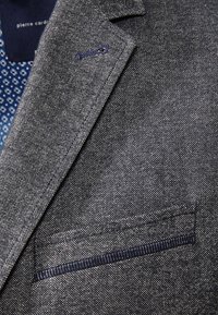 Szara marynarka z fakturowanej tkaniny, z klapą z wycięciem, kieszenią z ciemnoniebieskim akcentem oraz wzorzystą podszewką wewnętrzną.