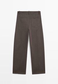 Mørkebrune bredbenede bukser lavet af bomuld. Har to baglommer med en søm-design og synlige sømme langs benene.