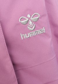 Roze stof met een gladde textuur, voorzien van een geborduurd logo in zilver met de tekst "hummel" en een gestileerd bijachtig embleem erboven.