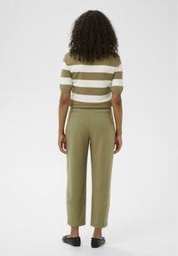 Haut en maille à rayures horizontales olive et blanches, manches courtes bouffantes. Pantalon olive vert ajusté avec coupe droite et poches arrière.