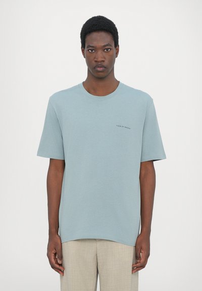 Helles blaues Baumwoll-T-Shirt mit kurzen Ärmeln, rundem Halsausschnitt und kleinen schwarzen Aufschrift "TIGER OF SWEDEN" auf der Brust. Rechteckige Form.