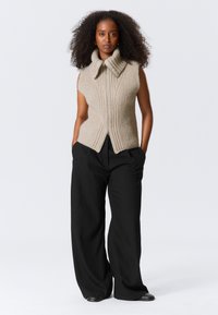 Beige geripptes Strickwesten mit hohem Kragen und Frontreißverschluss, kombiniert mit lockeren schwarzen Hosen und eleganten schwarzen Schuhen.