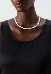 Pearl necklace with round, white beads, varying in size, resting on a dark top. Smooth texture; subtle sheen. Simple, classic design.