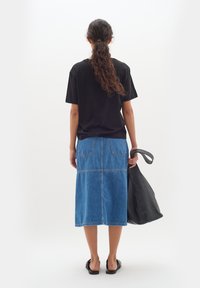Svart t-shirt med kort ärm, kombinerad med en blå denim midi-kjol som har två bakfickor och kontrasterande sömmar, medan den håller en svart handväska.