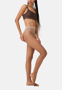 Collants transparents couleur tan avec une texture lisse et une taille haute, présentant des motifs rayés horizontaux au niveau des cuisses.