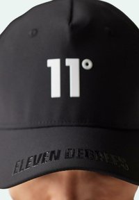 Gorra negra hecha de tela suave, con un destacado logo blanco "11°" en el frente y "ELEVEN DEGREES" grabado a lo largo del borde.