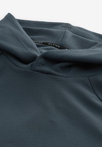 Chemise de sport texturée gris foncé avec un gros plan sur la zone du col et un seul bouton-pression noir au niveau de l'encolure.
